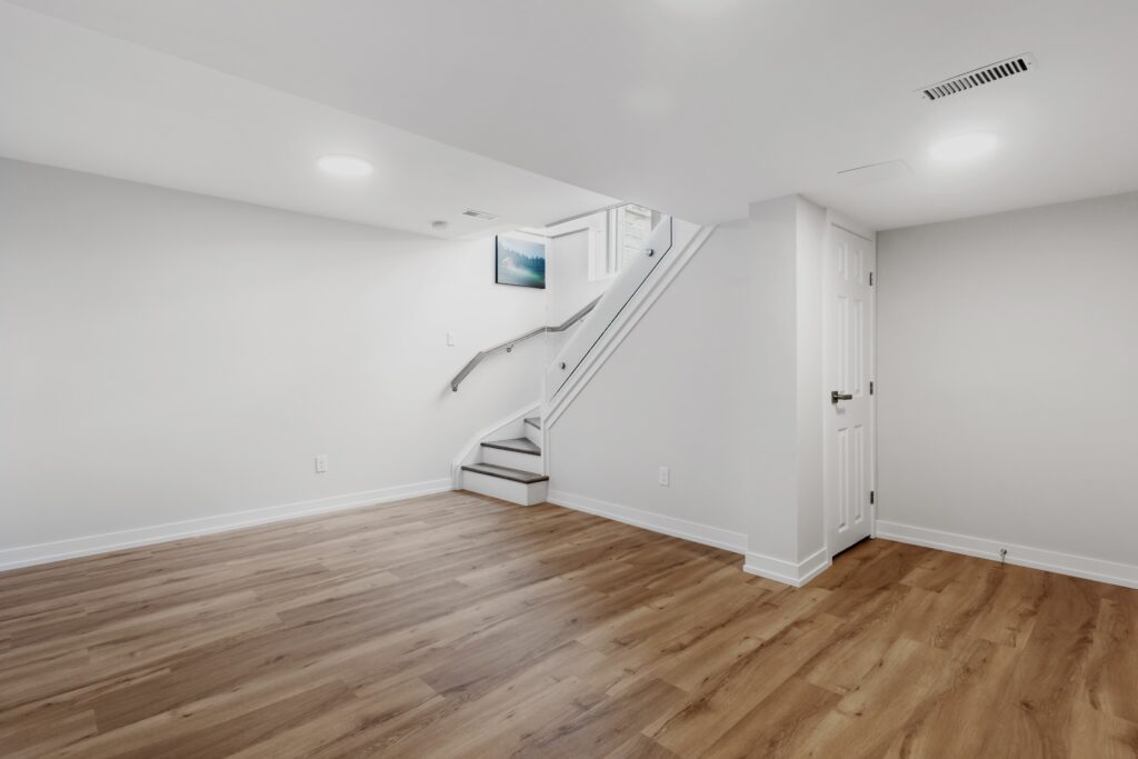 A basement space that has been remodeled. It has engineered wood floors, white walls, and a nice staircase leading down to the roomy basement area.